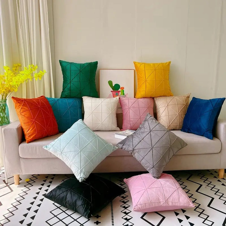 Assorted coloured cushion covers with geometric stitched lines displayed on a sofa and floor.