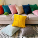 Assorted coloured cushion covers with geometric stitched lines displayed on a sofa and floor.