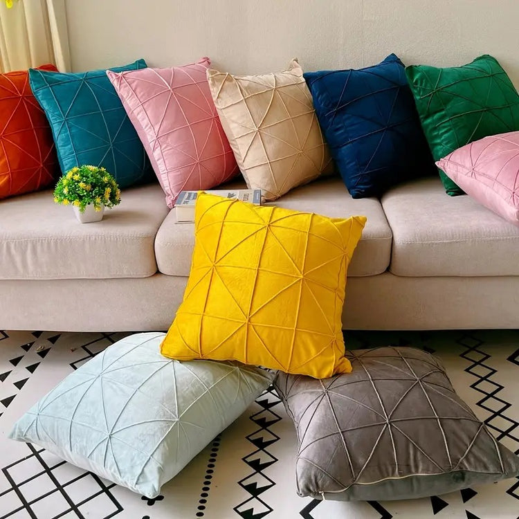 Assorted coloured cushion covers with geometric stitched lines displayed on a sofa and floor.