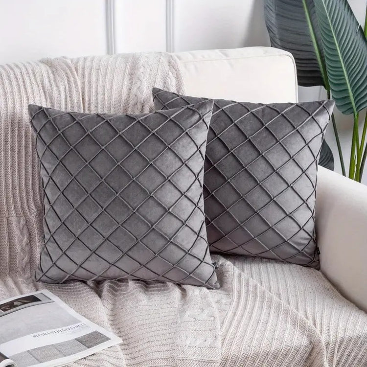 Two grey cushion covers with diamond stitching on a sofa.