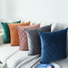 Assorted coloured cushion covers with diamond stitching arranged on a white sofa.