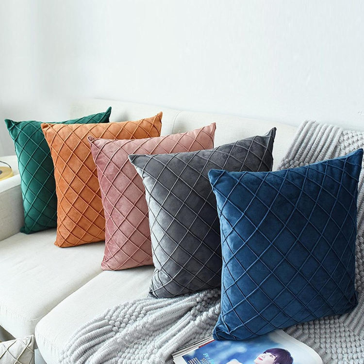 Assorted coloured cushion covers with diamond stitching arranged on a white sofa.