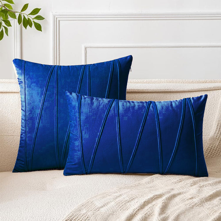 Blue square and rectangular cushion covers with angular stitched lines on a bed.