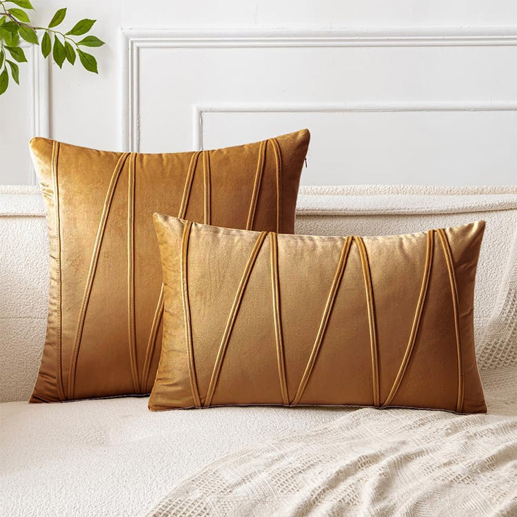 Tan square and rectangular cushion covers with angular stitched lines on a bed.