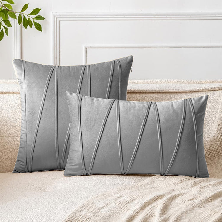 Grey square and rectangular cushion covers with angular stitched lines on a bed.