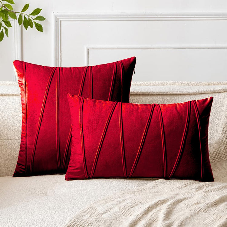 Red square and rectangular cushion covers with angular stitched lines on a bed.