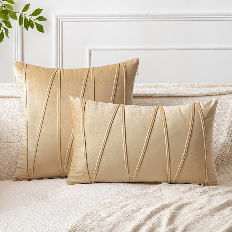 Cream square and rectangular cushion covers with angular stitched lines on a bed.