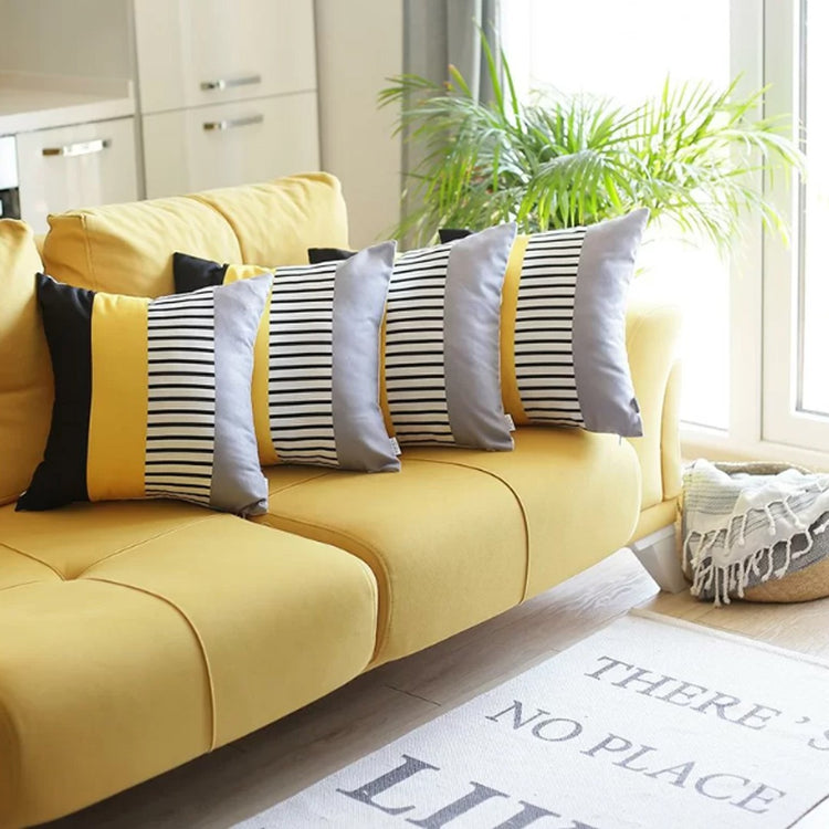 Black, yellow, grey and white striped cushion covers arranged on a yellow sofa.