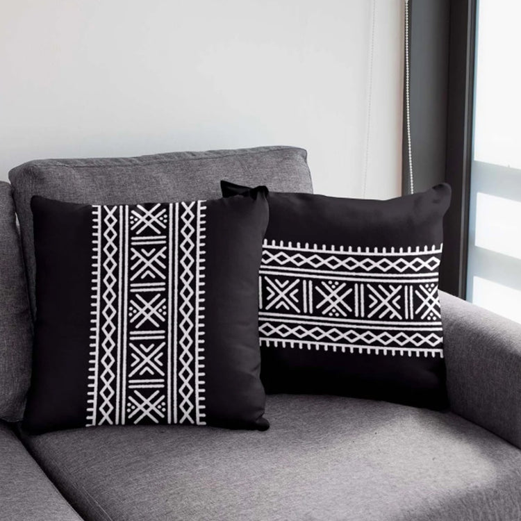 Black square and rectangular cushion covers with white geometric bands on a grey chair.