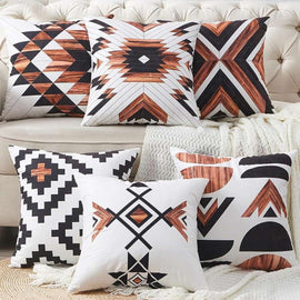 Six rust, black and cream geometric cushion covers displayed on a sofa.