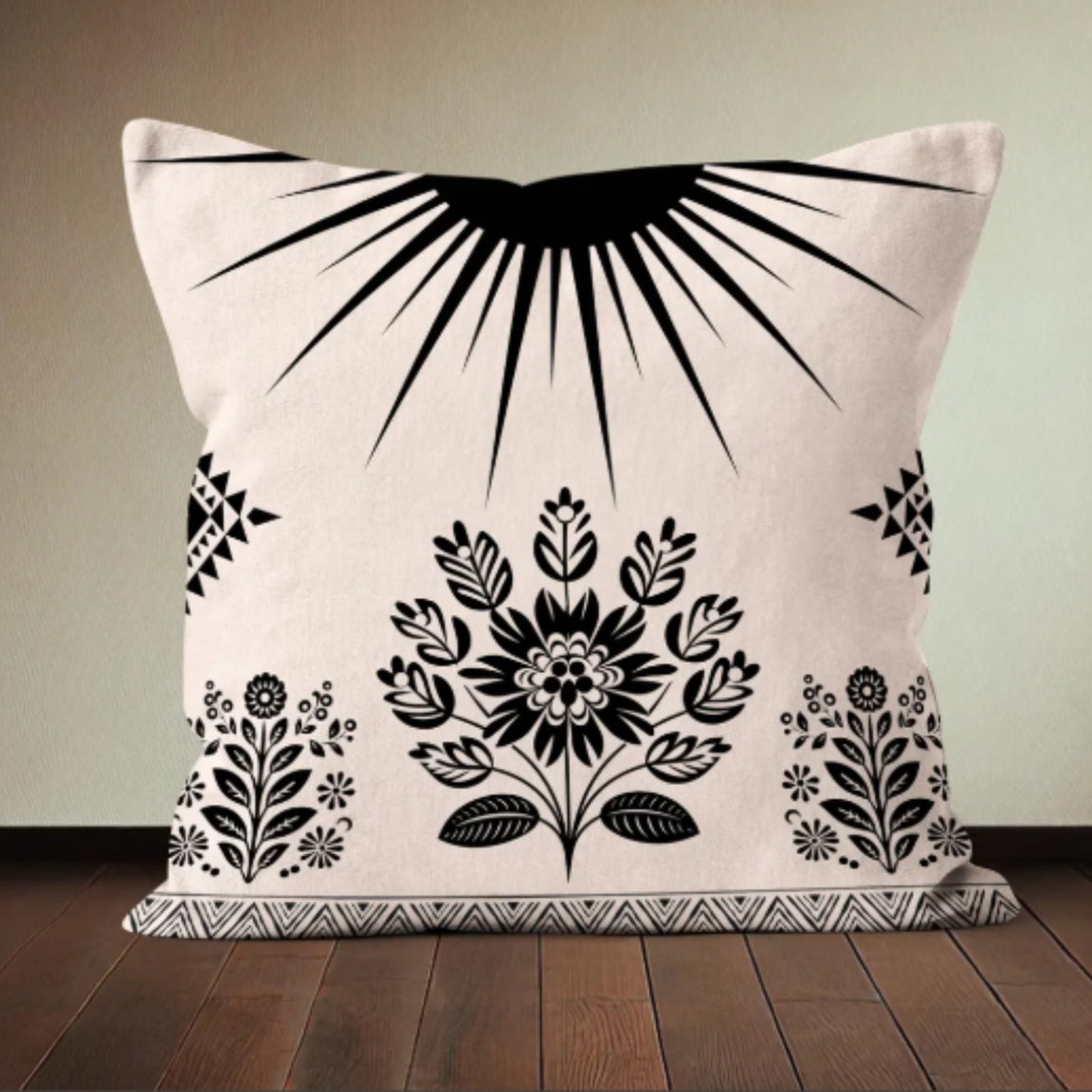 Cream cushion cover with black floral motifs beneath a large black sunburst.