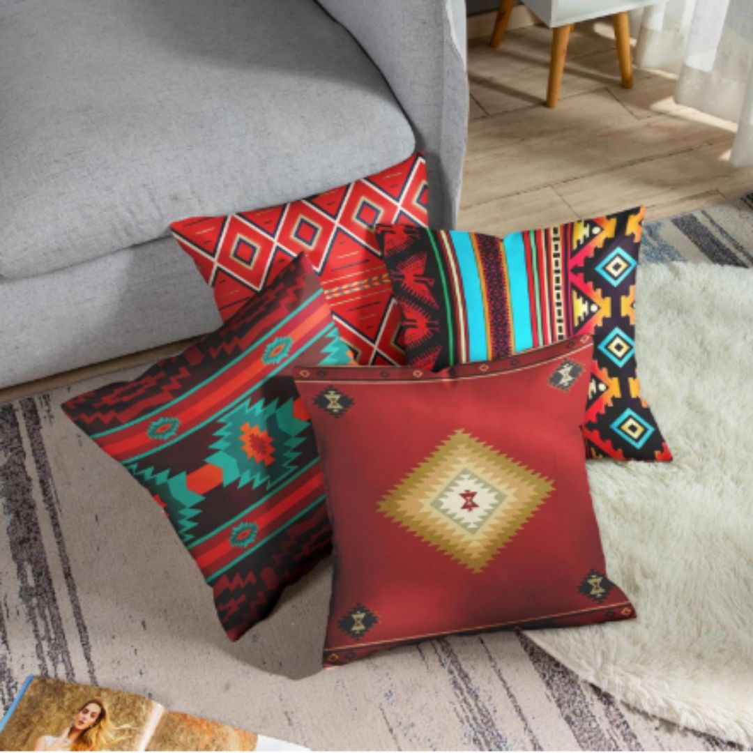 Four red, teal and multicoloured geometric cushion covers arranged on a rug beside a sofa.