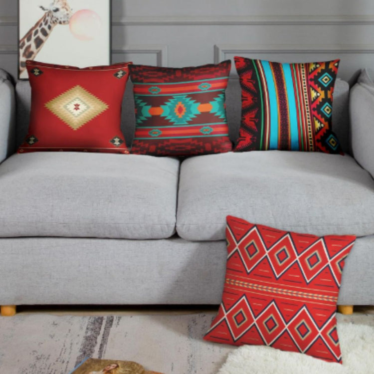 Four red and teal geometric cushion covers arranged on a gray sofa and the floor
