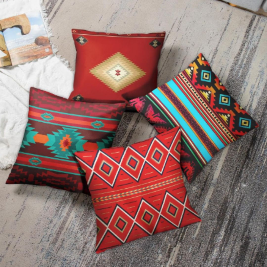 Four red, teal and multicoloured geometric cushion covers arranged on a rug beside a sofa.