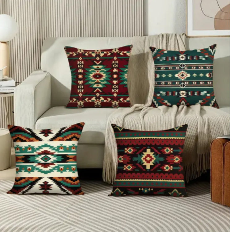 Four red, teal and cream geometric cushion covers displayed in a living room.