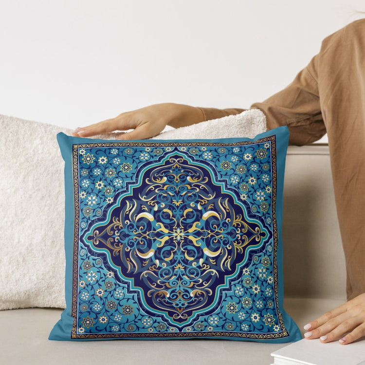 Blue cushion cover with an intricate gold coloured floral medallion held on a sofa.