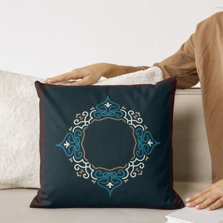 Dark teal cushion cover with a blue and gold coloured circular ornament held on a sofa.