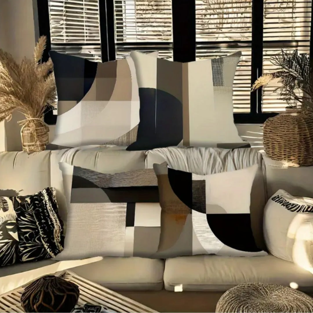 Four black, beige and grey abstract geometric cushion covers arranged on a sofa.