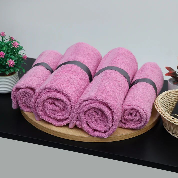 Pink cotton towels rolled and arranged on a tray.