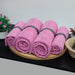 Pink cotton towels rolled and arranged on a tray.