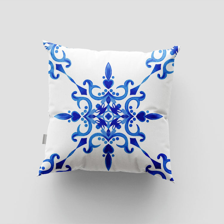 White cushion cover with an ornate blue central star and curling corner flourishes.