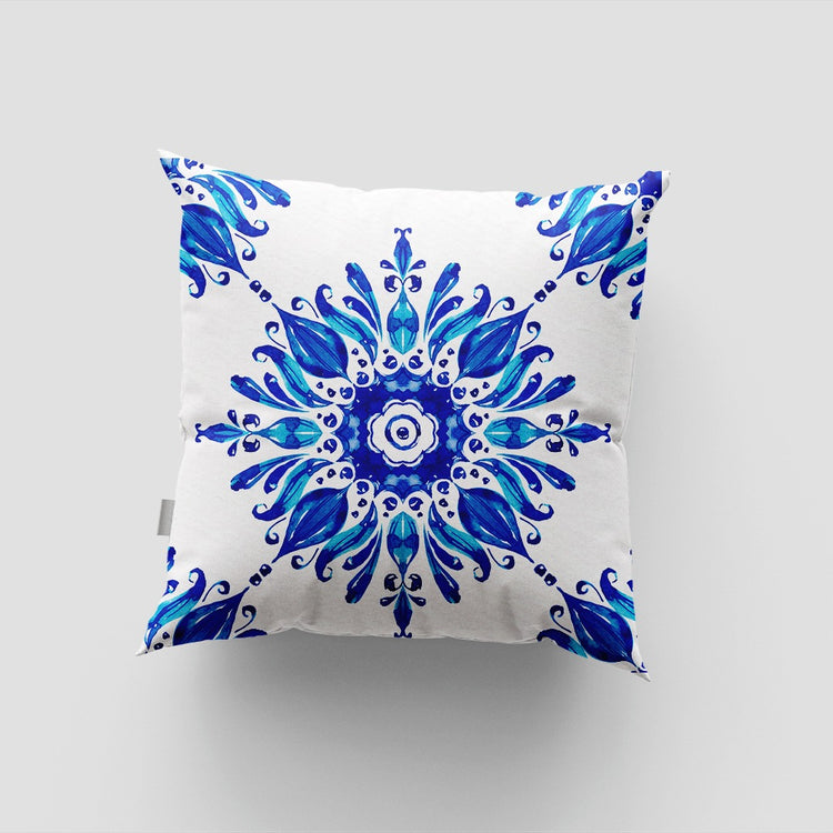 White cushion cover with a large blue floral medallion and small corner motifs.