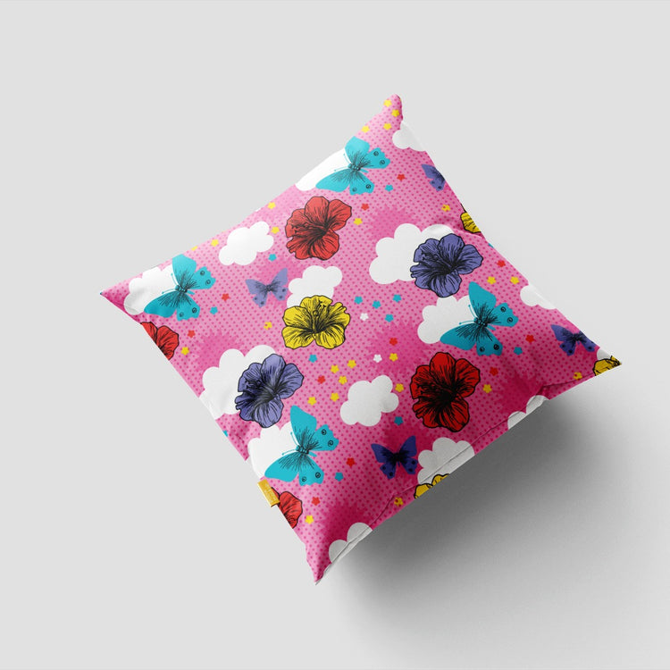Pink cushion cover with scattered bright flowers and dark leaf-like shapes.