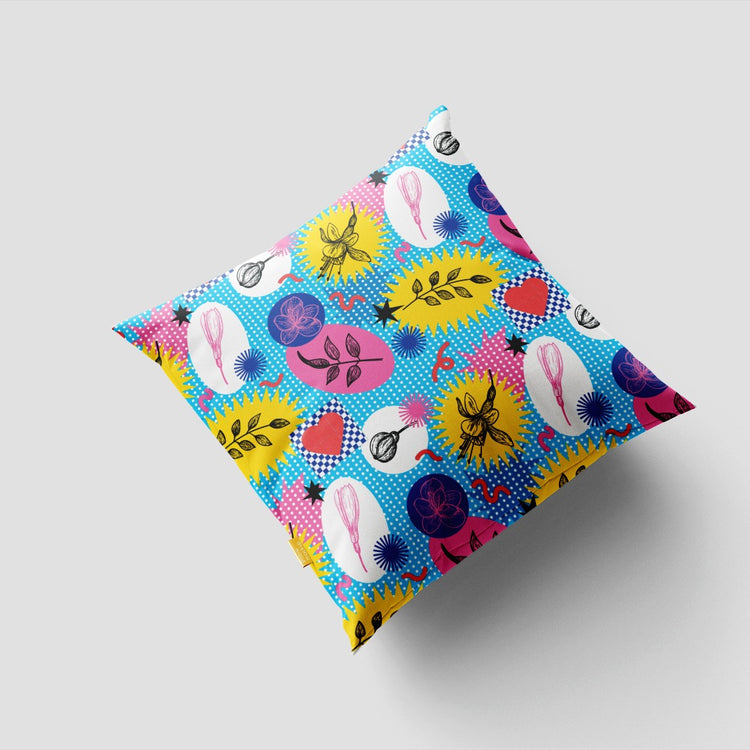 Blue cushion cover with bright pink and yellow abstract shapes, dots and leaf-like marks.