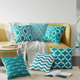 Teal and white geometric cushion covers arranged on a mustard sofa and rug.