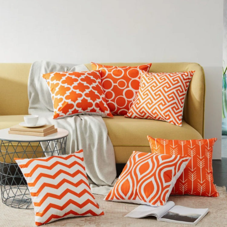 Orange and white geometric cushion covers arranged on a mustard sofa and rug.