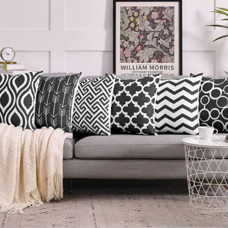 Black and white geometric cushion covers arranged on a grey sofa and the floor.