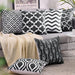 Black and white geometric cushion covers arranged on a grey sofa and the floor.