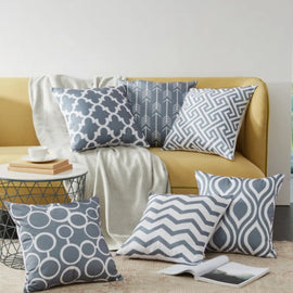 Grey and white geometric cushion covers displayed on a mustard sofa and rug.