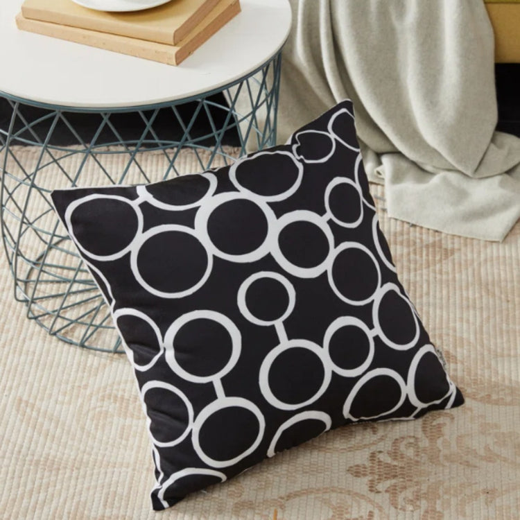 Black cushion cover with interlocking white circles beside a wire table.