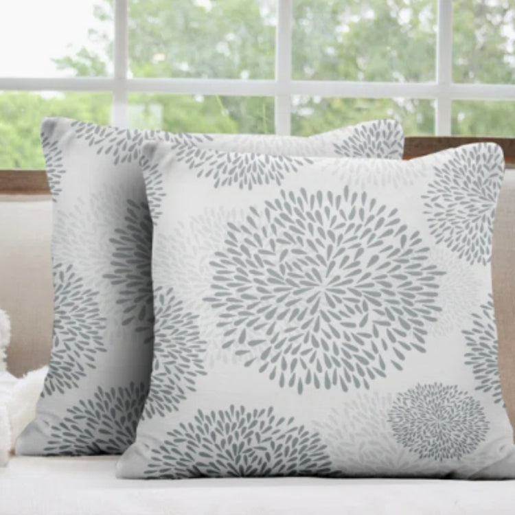 Two white cushion covers with pale grey circular floral patterns on a sofa.