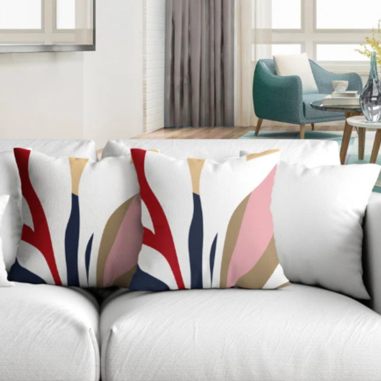 Two cream cushion covers with red, pink and navy abstract shapes displayed on a sofa.