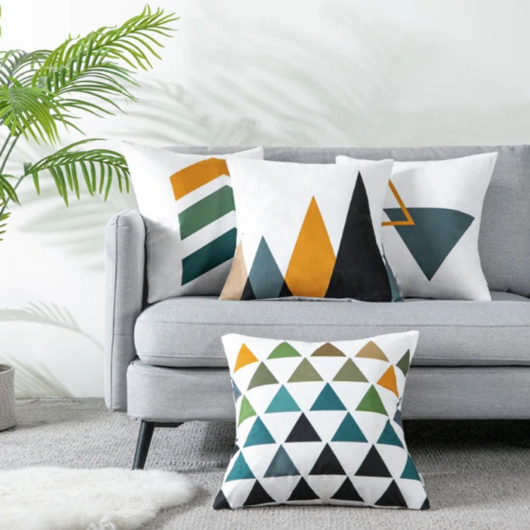 Four white cushion covers with teal, mustard and grey geometric shapes on a sofa and floor.