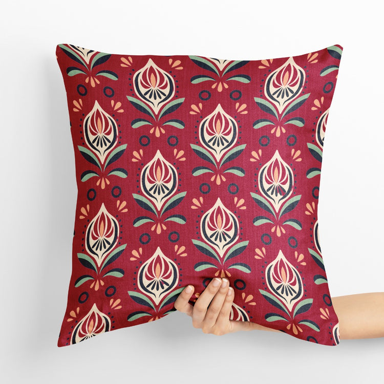 Red cushion cover with repeating cream and gold coloured botanical motifs.