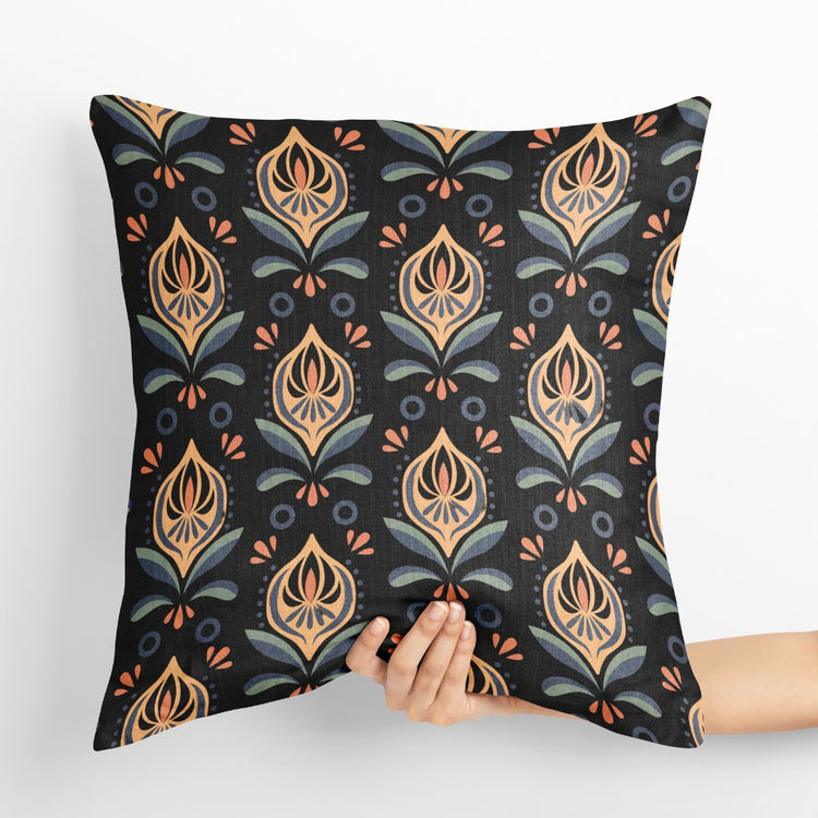 Dark charcoal cushion cover with repeating cream and gold coloured botanical motifs.