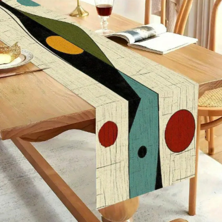 Close view of a cream table runner with black, teal, yellow and red abstract shapes.