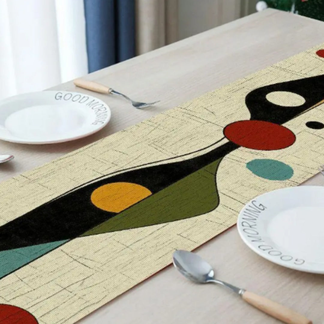 Close view of a cream table runner with black, teal, yellow and red abstract shapes.