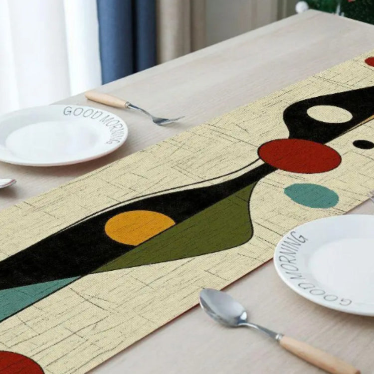 Close view of a cream table runner with black, teal, yellow and red abstract shapes.