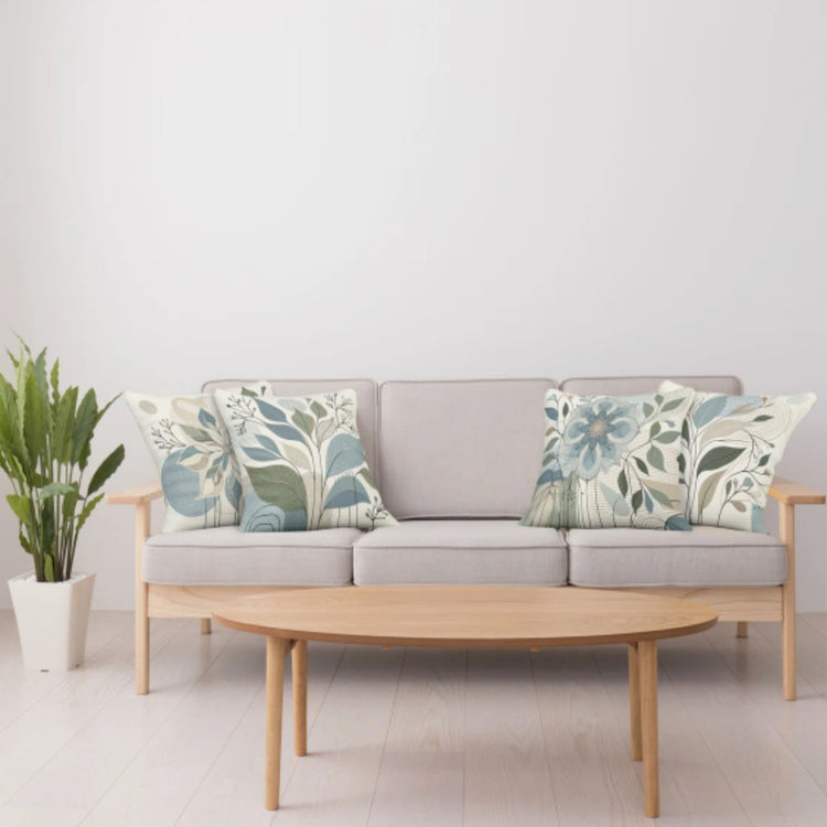 Pale blue and green botanical cushion covers arranged on a light sofa.