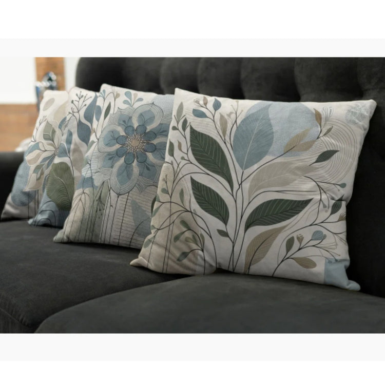 Close view of cream cushion covers with muted blue flowers and green leaves on a dark sofa.