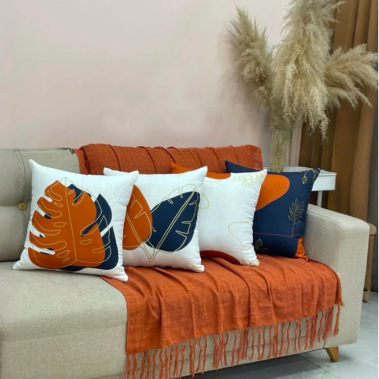 Rust, navy and cream cushion covers with bold leaf designs arranged on a sofa.
