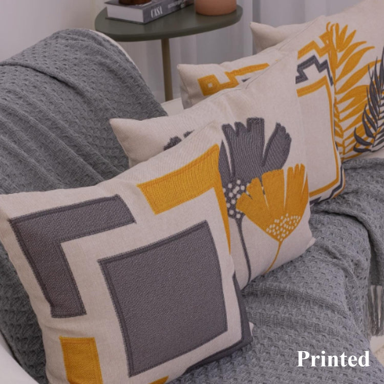 Grey, white and mustard cushion covers with geometric frames and leaf designs on a sofa.