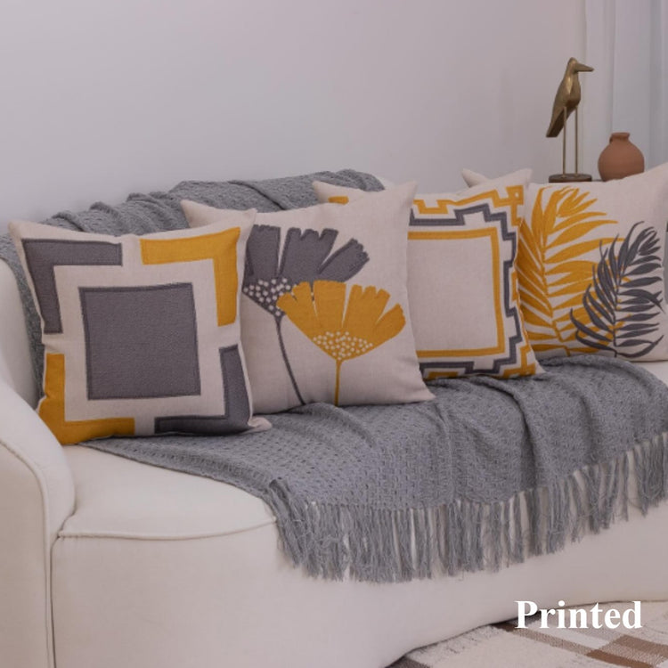 Grey, white and mustard cushion covers with geometric frames and leaf designs on a sofa.