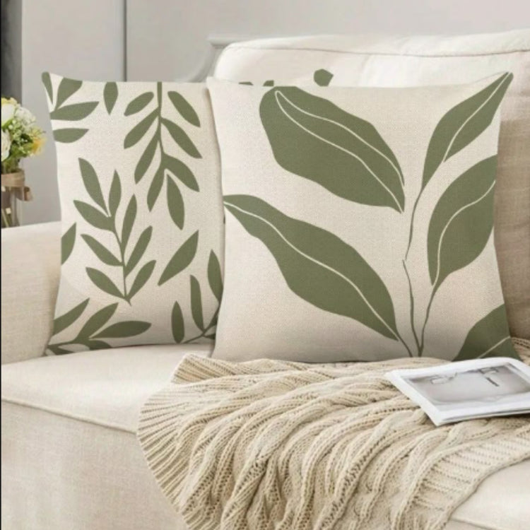 Two cream cushion covers with olive green leafy stems on a sofa.