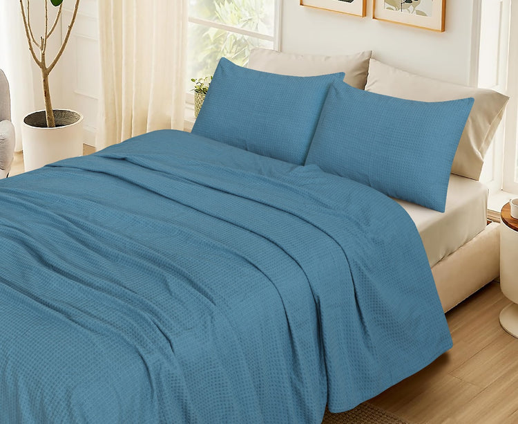 Teal textured blanket with matching pillow covers displayed on a bed.