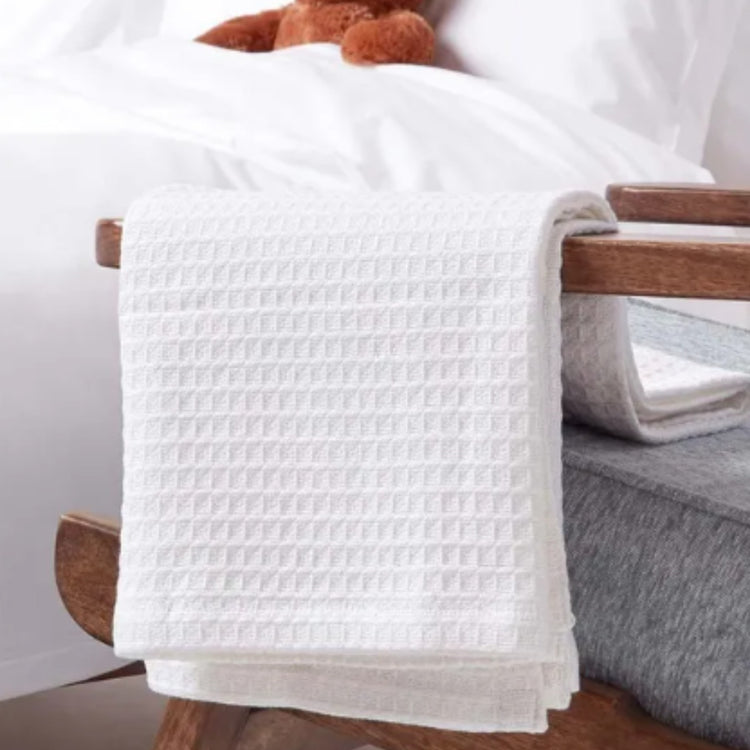Folded white waffle-textured blanket draped over a wooden chair arm beside a bed